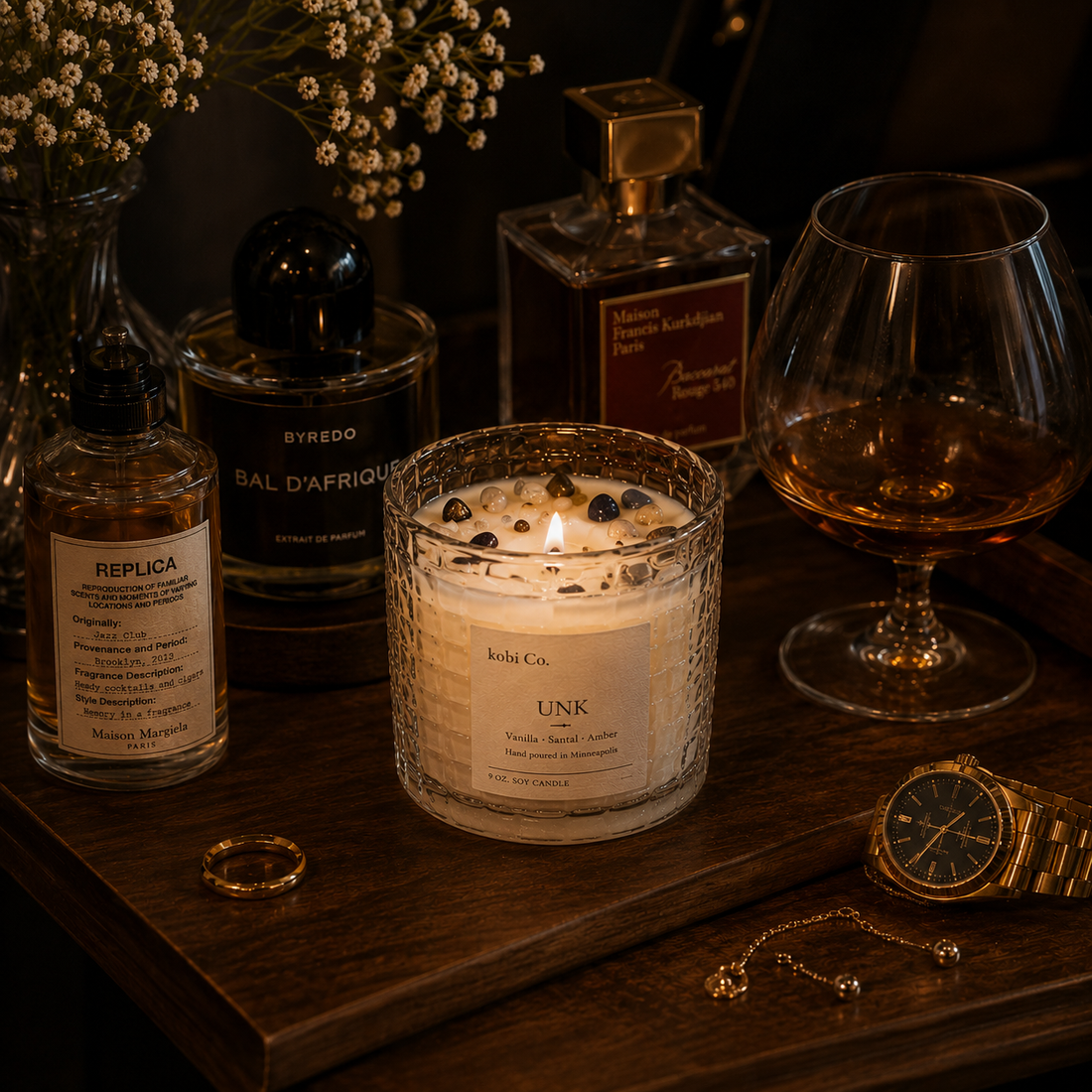 Candle, perfume bottles, glass of whiskey, and other items on a wooden surface.